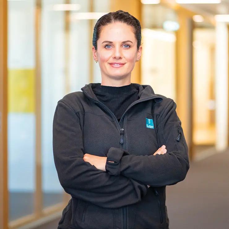 Franziska Beck mit verschränkten Armen im Flur von Sutter Medizintechnik – Ausbilderin in der Feinmechanik.