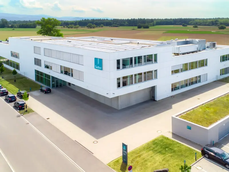 Luftaufnahme des modernen Firmengebäudes von Sutter Medizintechnik in Emmendingen mit Blick auf das Umfeld und angrenzende Felder.        ChatGPT fragen