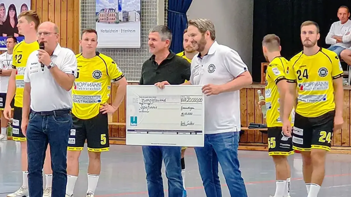 Bert Sutter übergibt symbolischen Spendenscheck an SpoFunnis bei einem Handball-Heimspiel – Engagement für Kinder- und Jugendarbeit in der Region.