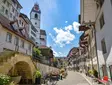 Historische Gasse in der Altstadt von Aarau, Schweiz, mit Blick auf den markanten Stadtturm und charmanten Fachwerkhäusern an einem sonnigen Tag.