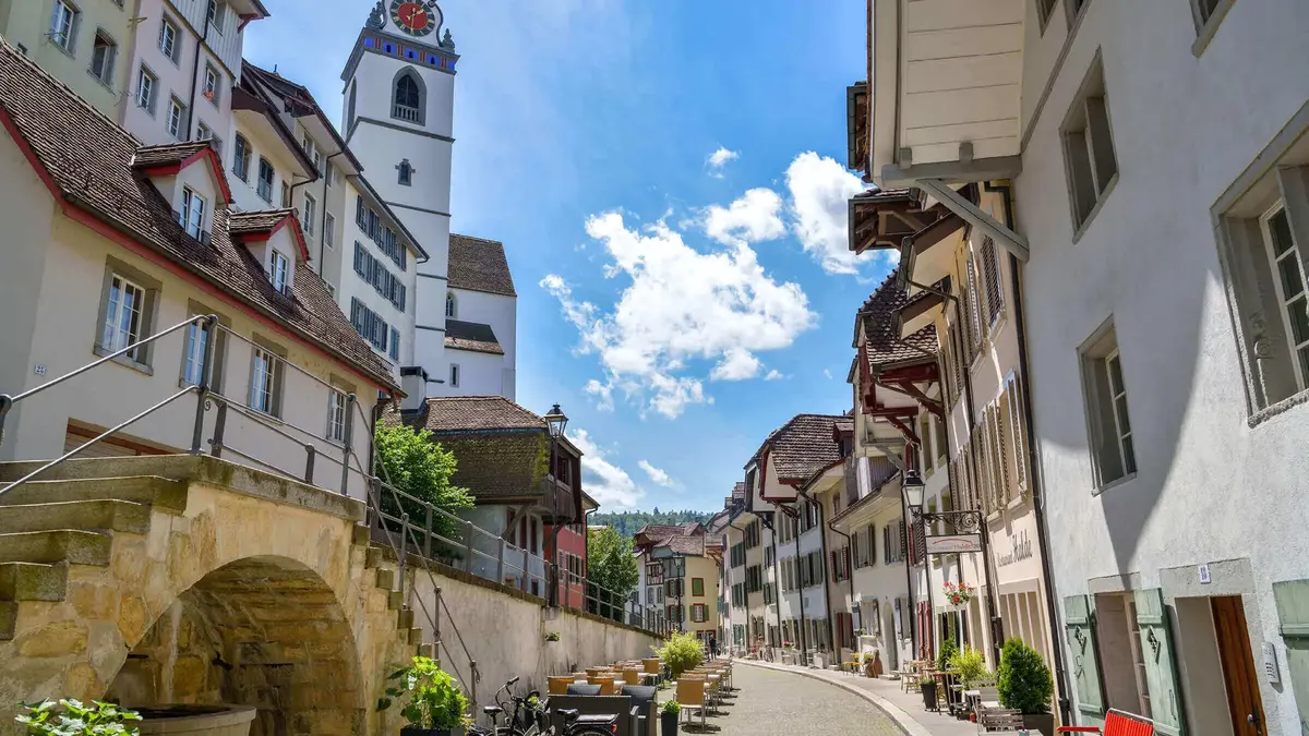 Historische Gasse in der Altstadt von Aarau, Schweiz, mit Blick auf den markanten Stadtturm und charmanten Fachwerkhäusern an einem sonnigen Tag.