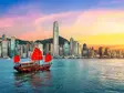 Traditionelles chinesisches Junkboot mit roten Segeln fährt vor der Skyline von Hongkong bei farbenprächtigem Sonnenuntergang über das Wasser.        