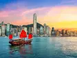 Traditionelles chinesisches Junkboot mit roten Segeln fährt vor der Skyline von Hongkong bei farbenprächtigem Sonnenuntergang über das Wasser.        