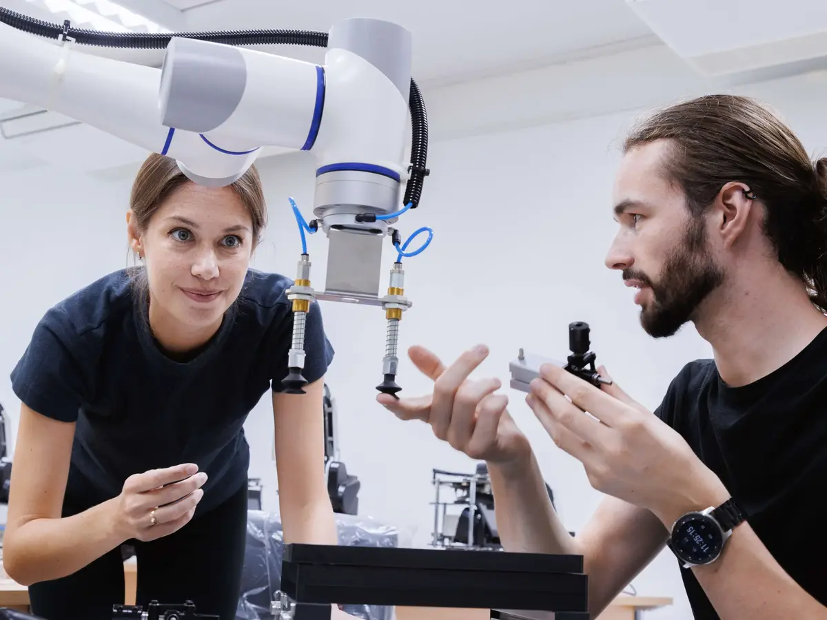 Two professionals inspecting a collaborative robotic arm in a technical development environment.
