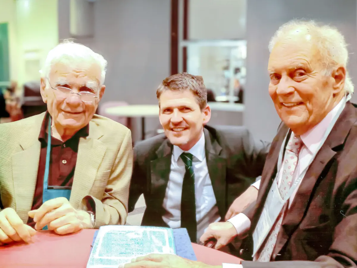 Three people seated at a table during an event in a modern indoor setting.