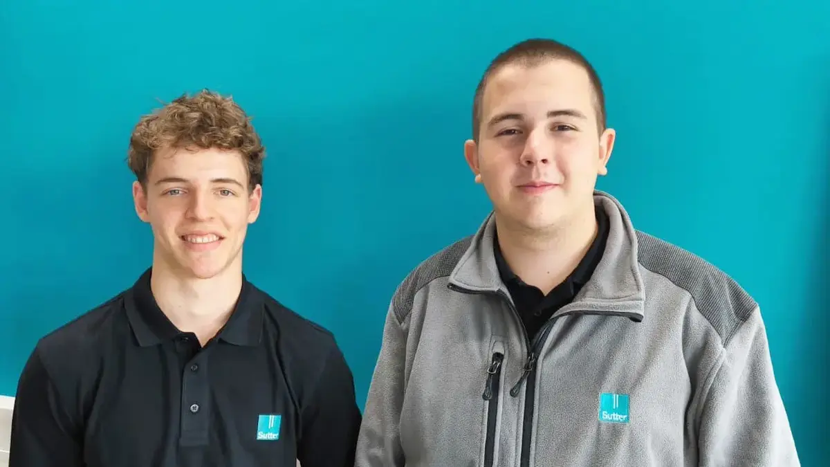 Zwei Personen mit Firmenkleidung und lächelnd vor türkisfarbenem Hintergrund