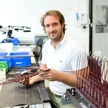 Ein Mitarbeiter von Sutter Medizintechnik prüft chirurgische Instrumente in der Qualitätskontrolle und blickt freundlich in die Kamera.