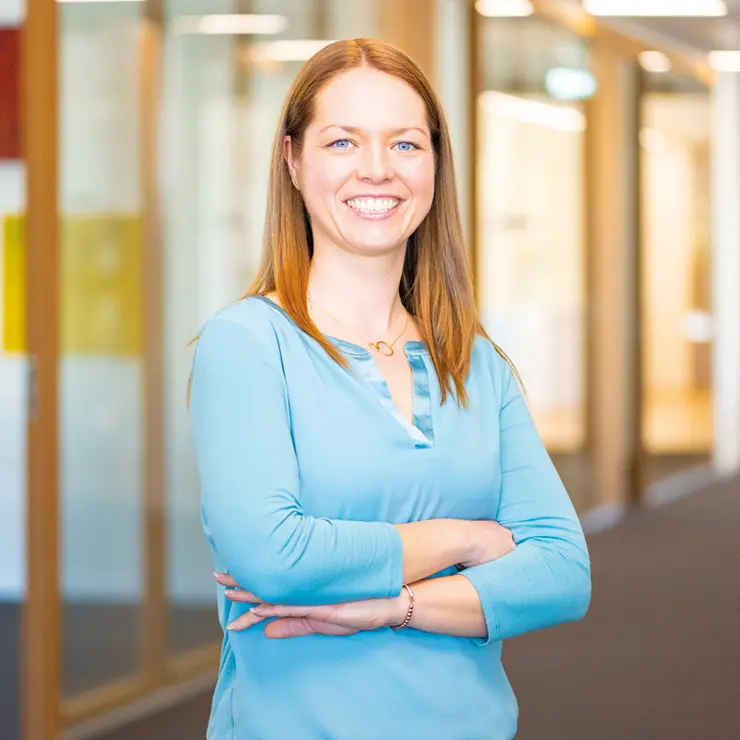 Eine lächelnde Mitarbeiterin von Sutter Medizintechnik steht mit verschränkten Armen im hellen Büroflur und trägt eine hellblaue Bluse.